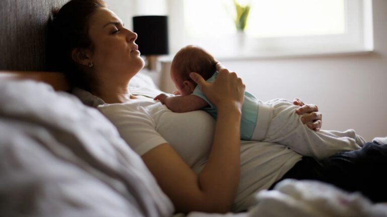 Wochenbett früher und heute: Mutter ruht im Bett mit ihrem Neugeborenen auf der Brust
